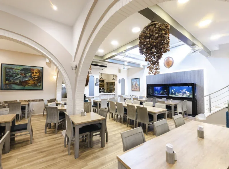 Salón del restaurante con arcos blancos, mesas de madera y acuario en Pescocentro Búcaro, Bucaramanga